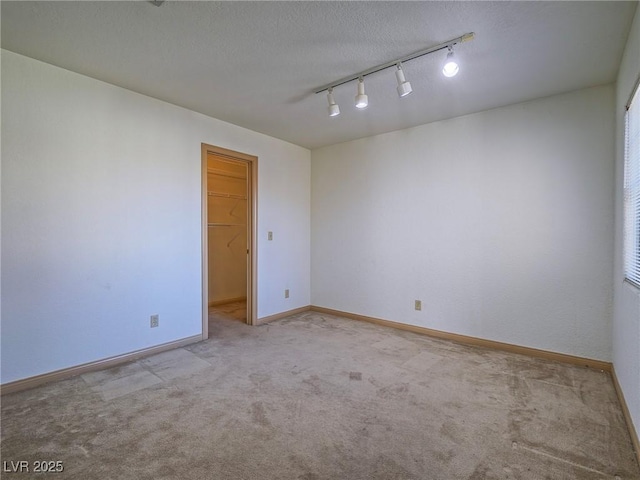 unfurnished room featuring a textured ceiling, track lighting, and light colored carpet