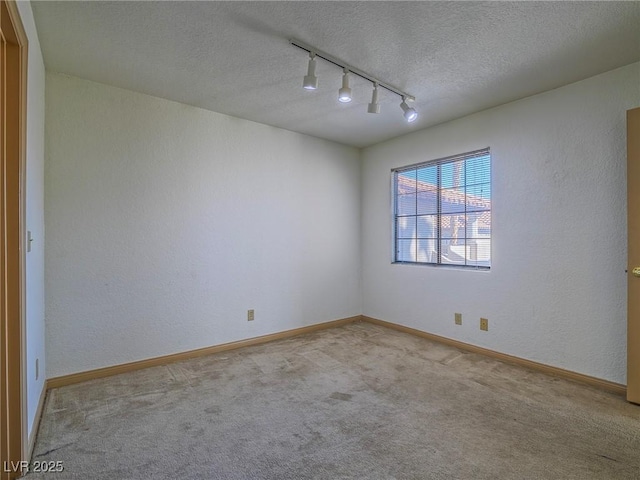 empty room with light carpet, track lighting, and a textured ceiling