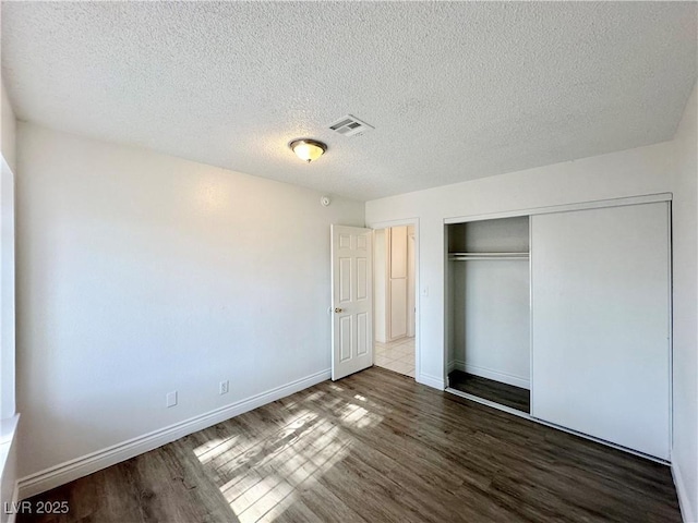 unfurnished bedroom featuring a textured ceiling, a closet, and dark hardwood / wood-style floors