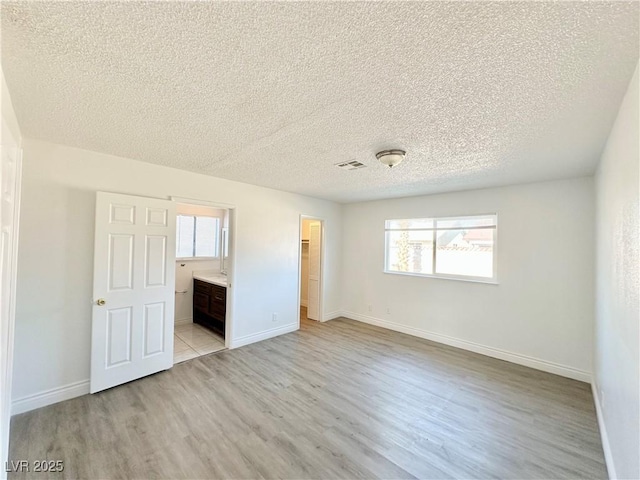 unfurnished bedroom with a textured ceiling, ensuite bathroom, light wood-type flooring, and multiple windows