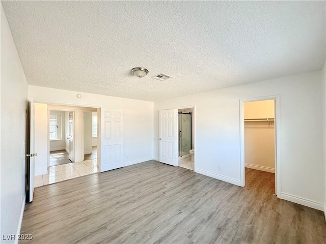 unfurnished bedroom with a textured ceiling, a walk in closet, connected bathroom, light hardwood / wood-style floors, and a closet