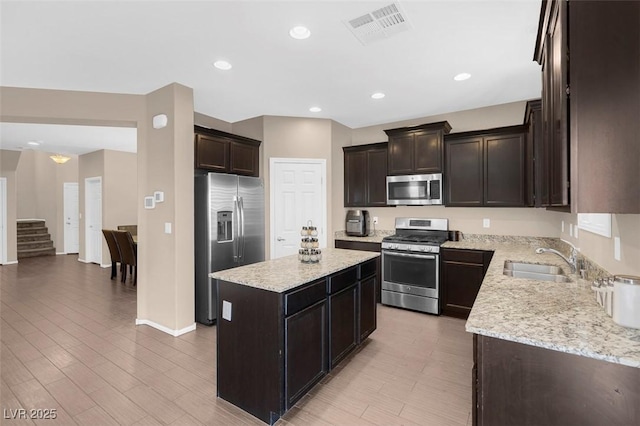 kitchen featuring light stone countertops, appliances with stainless steel finishes, a kitchen island, sink, and dark brown cabinets