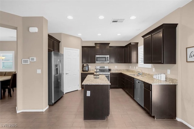 kitchen featuring dark brown cabinetry, appliances with stainless steel finishes, a center island, sink, and light stone counters