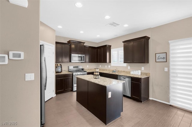 kitchen with stainless steel appliances, a center island, light stone counters, dark brown cabinetry, and sink