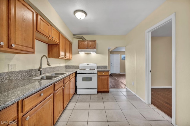 kitchen with light tile patterned floors, sink, white gas stove, and dark stone counters