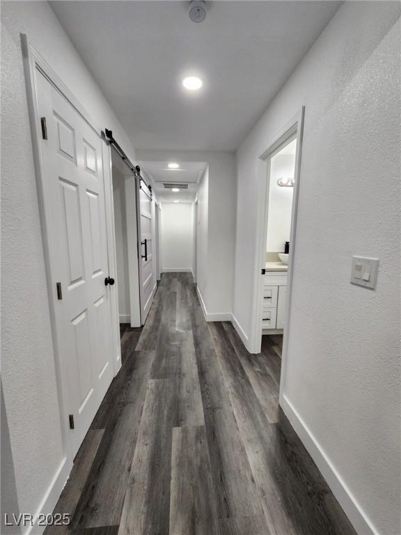 corridor with dark wood-type flooring and a barn door