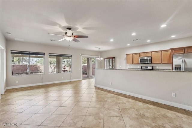 kitchen with light tile patterned floors, ceiling fan with notable chandelier, appliances with stainless steel finishes, brown cabinetry, and pendant lighting