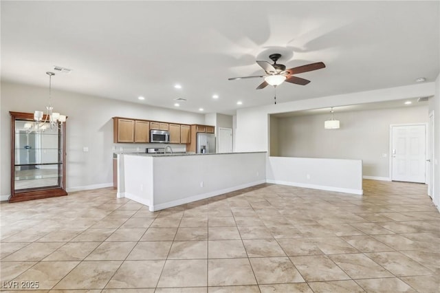 kitchen with stainless steel appliances, brown cabinetry, decorative light fixtures, and ceiling fan with notable chandelier