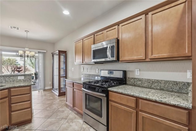 kitchen featuring stainless steel appliances, brown cabinets, visible vents, and light stone countertops