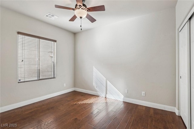 empty room with dark wood-style floors, baseboards, visible vents, and ceiling fan