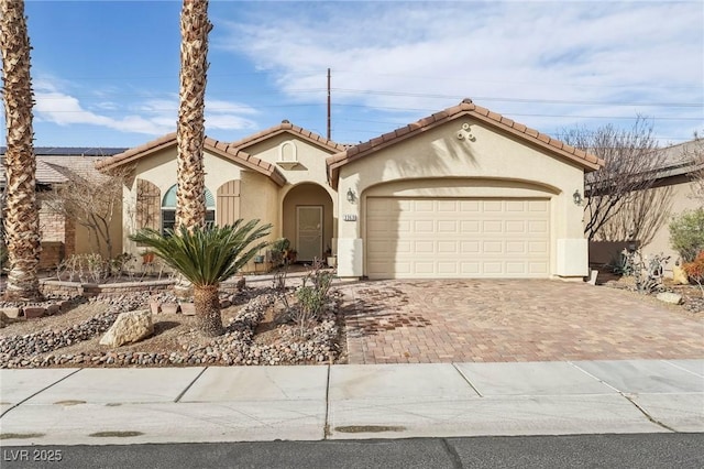 mediterranean / spanish home with a garage, a tile roof, decorative driveway, and stucco siding