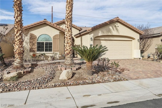 mediterranean / spanish home featuring an attached garage, a tiled roof, decorative driveway, and stucco siding