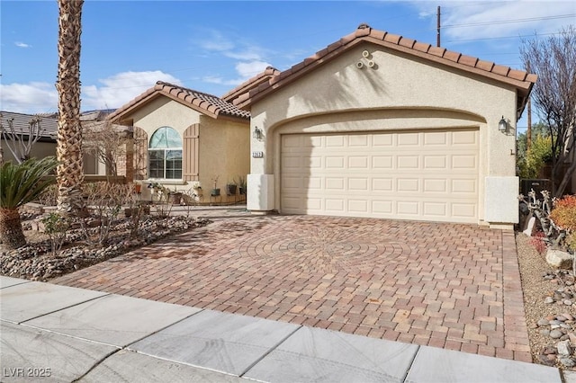 mediterranean / spanish house with a garage, decorative driveway, a tiled roof, and stucco siding