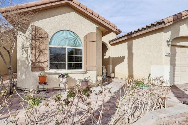 view of side of home featuring a garage, a tiled roof, and stucco siding