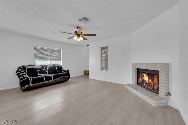 sitting room featuring ceiling fan, a brick fireplace, a textured ceiling, and light hardwood / wood-style flooring