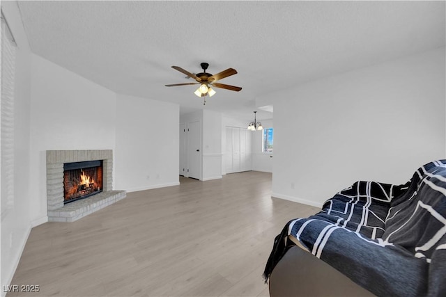 living room with a brick fireplace, ceiling fan with notable chandelier, a textured ceiling, and hardwood / wood-style flooring