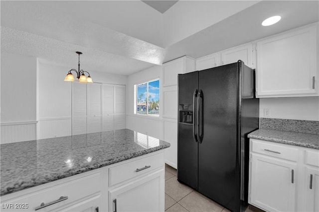 kitchen with decorative light fixtures, black fridge, light tile patterned flooring, stone counters, and white cabinets