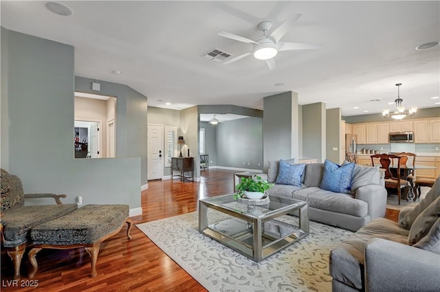 living room with ceiling fan with notable chandelier and light wood-type flooring