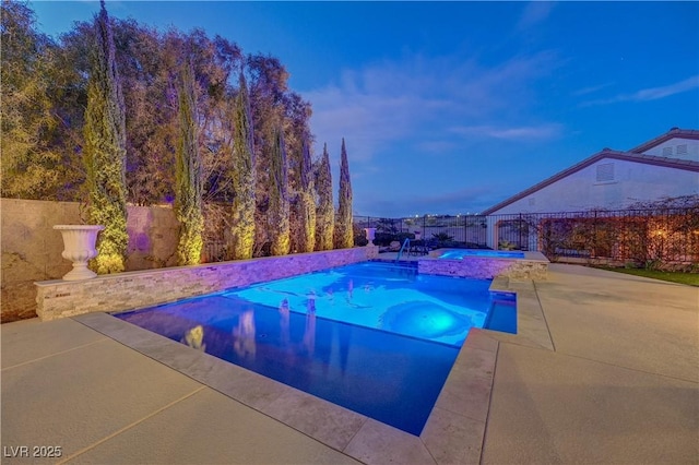 pool at dusk with an in ground hot tub and a patio