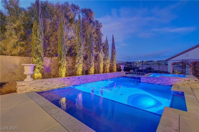 pool at dusk with a patio area and an in ground hot tub