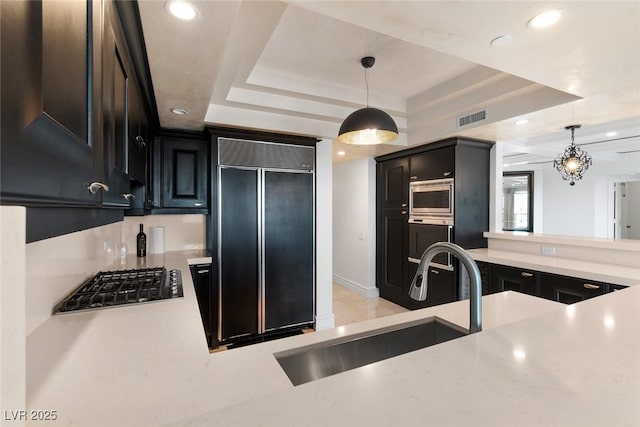 kitchen with a raised ceiling, light countertops, decorative light fixtures, and built in appliances