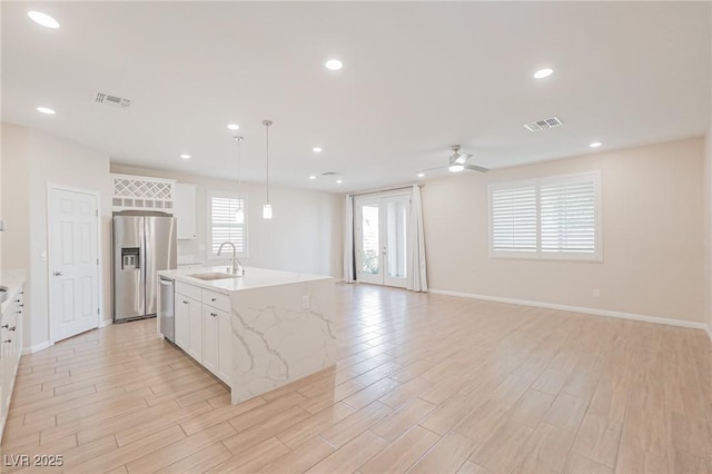 kitchen with white cabinets, appliances with stainless steel finishes, sink, hanging light fixtures, and a center island with sink