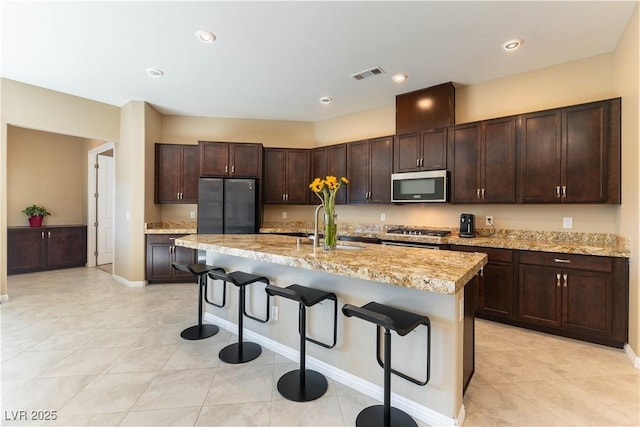 kitchen featuring a breakfast bar, stainless steel appliances, a kitchen island with sink, dark brown cabinetry, and sink