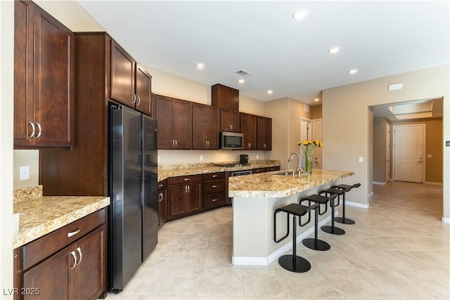 kitchen featuring a center island with sink, stainless steel appliances, dark brown cabinets, a breakfast bar, and sink