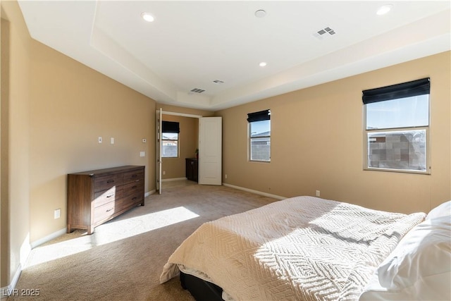 bedroom with light colored carpet and a tray ceiling