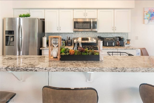 kitchen with light stone counters, a kitchen breakfast bar, white cabinetry, and appliances with stainless steel finishes