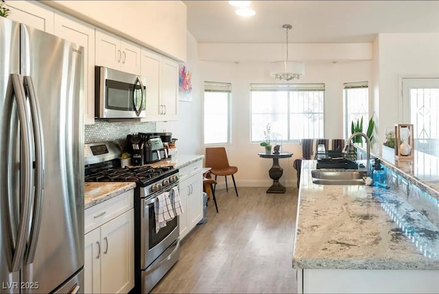 kitchen featuring pendant lighting, sink, light stone countertops, appliances with stainless steel finishes, and white cabinets