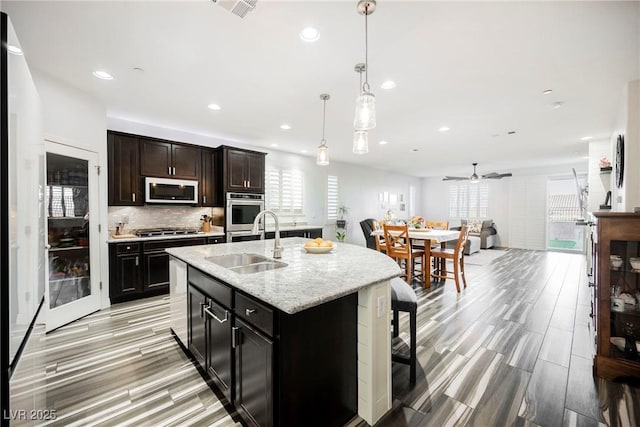 kitchen with sink, ceiling fan, stainless steel appliances, a center island with sink, and decorative light fixtures