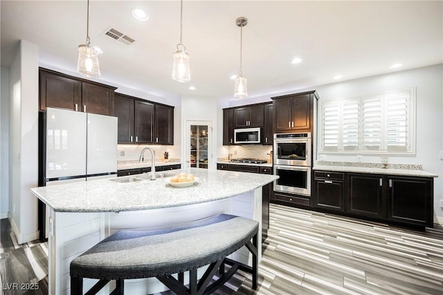 kitchen featuring sink, hanging light fixtures, an island with sink, stainless steel appliances, and decorative backsplash