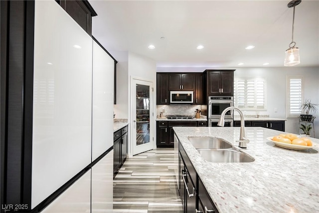 kitchen featuring pendant lighting, sink, backsplash, stainless steel appliances, and light stone countertops