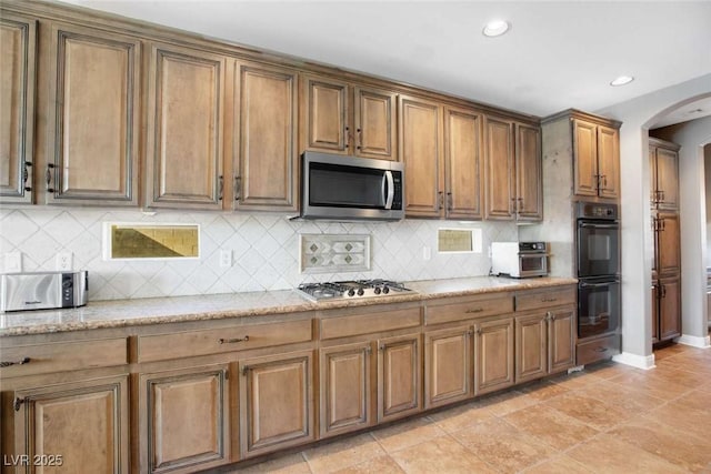 kitchen with decorative backsplash, light stone countertops, and appliances with stainless steel finishes