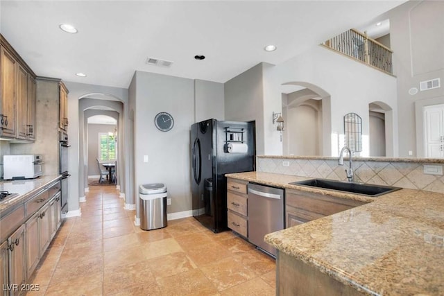 kitchen with appliances with stainless steel finishes, backsplash, light stone counters, and sink