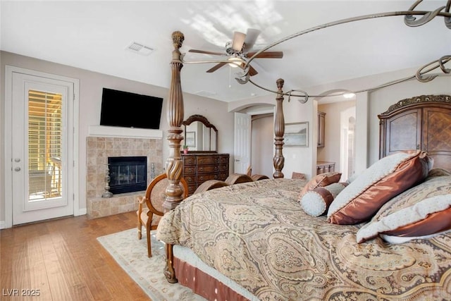 bedroom featuring ceiling fan, access to exterior, a tile fireplace, and light hardwood / wood-style flooring