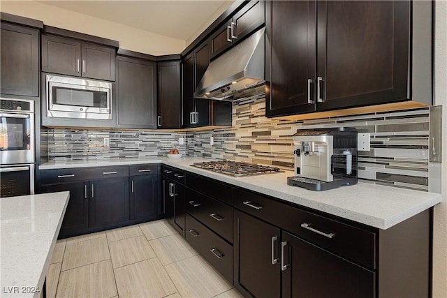 kitchen featuring light stone countertops, backsplash, appliances with stainless steel finishes, and dark brown cabinets