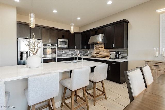 kitchen with stainless steel appliances, decorative backsplash, dark brown cabinets, pendant lighting, and sink