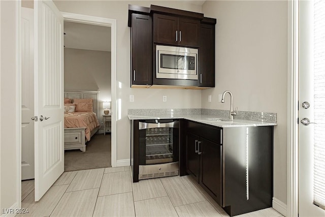 kitchen with stainless steel microwave, wine cooler, sink, and light stone counters