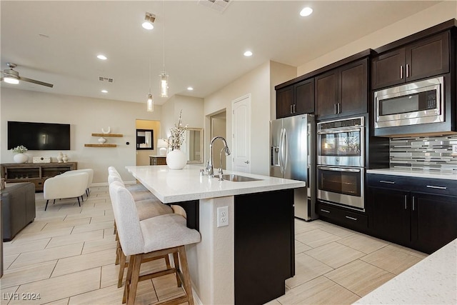 kitchen featuring a kitchen bar, a center island with sink, appliances with stainless steel finishes, decorative light fixtures, and sink