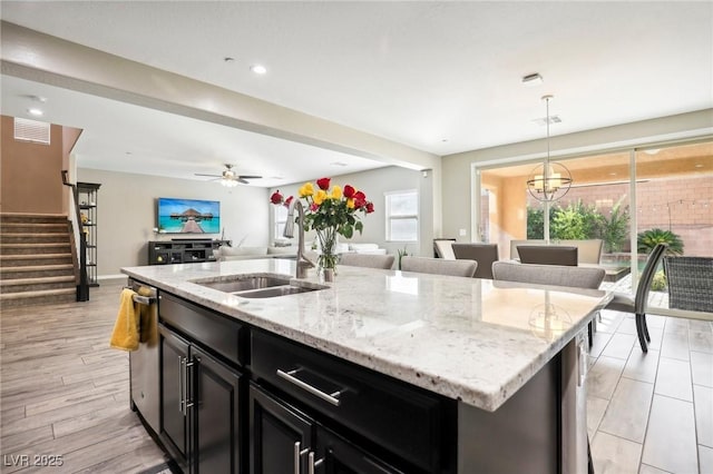 kitchen with decorative light fixtures, sink, an island with sink, and light stone counters