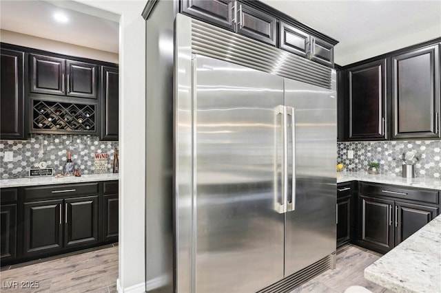 kitchen with light stone counters, backsplash, stainless steel built in fridge, and light hardwood / wood-style flooring