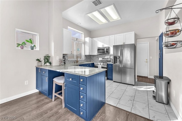 kitchen featuring sink, blue cabinetry, white cabinetry, stainless steel appliances, and kitchen peninsula