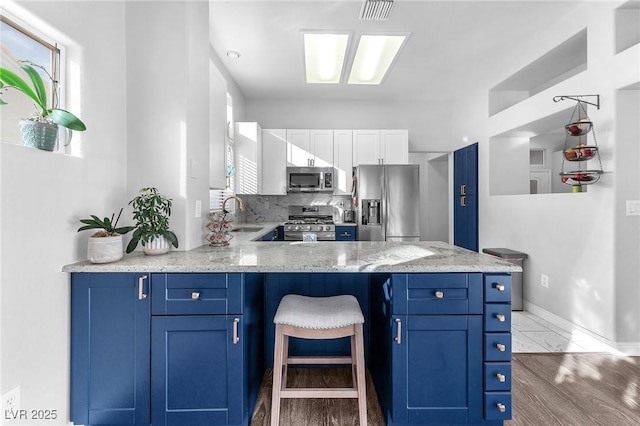 kitchen with light stone counters, blue cabinetry, white cabinets, and appliances with stainless steel finishes