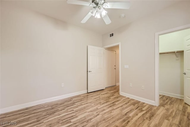 unfurnished bedroom featuring ceiling fan, light hardwood / wood-style floors, a closet, and a walk in closet