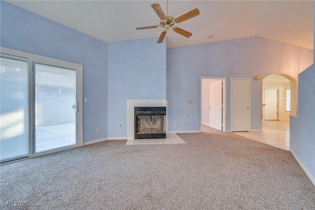 unfurnished living room with vaulted ceiling, light carpet, a textured ceiling, ceiling fan, and a tiled fireplace