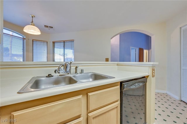 kitchen featuring light brown cabinetry, dishwasher, sink, and hanging light fixtures