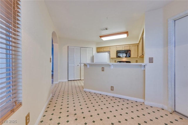 kitchen featuring light brown cabinetry, a breakfast bar area, and white fridge