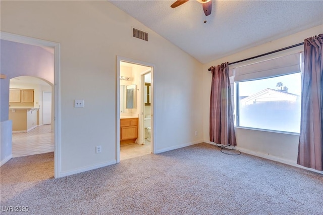 unfurnished bedroom featuring connected bathroom, vaulted ceiling, a textured ceiling, ceiling fan, and light colored carpet